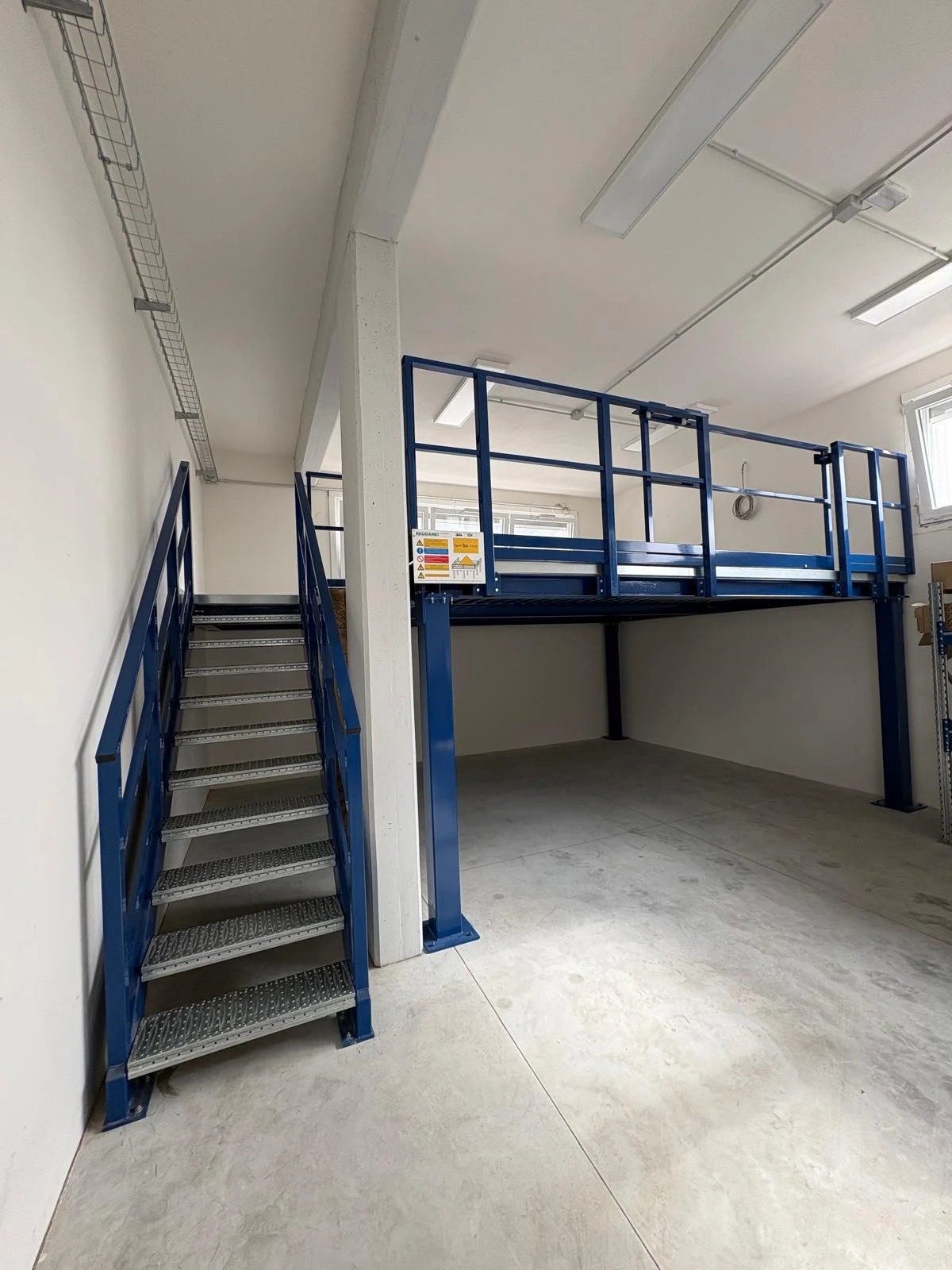 Scala metallica con gradini grigliati che conduce a un soppalco in acciaio blu.