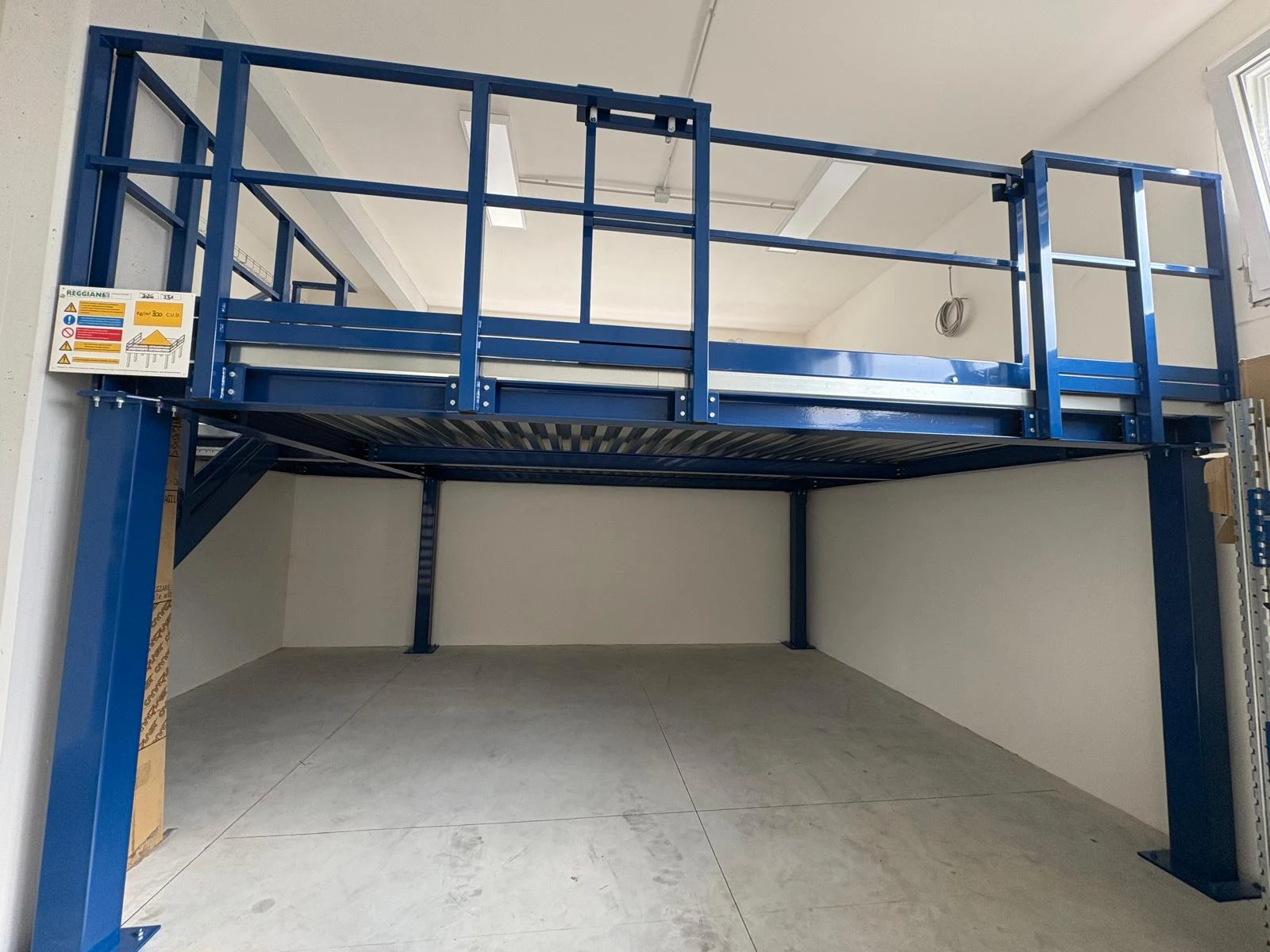 Vista frontale di un soppalco in acciaio blu con parapetto e spazio sottostante.
